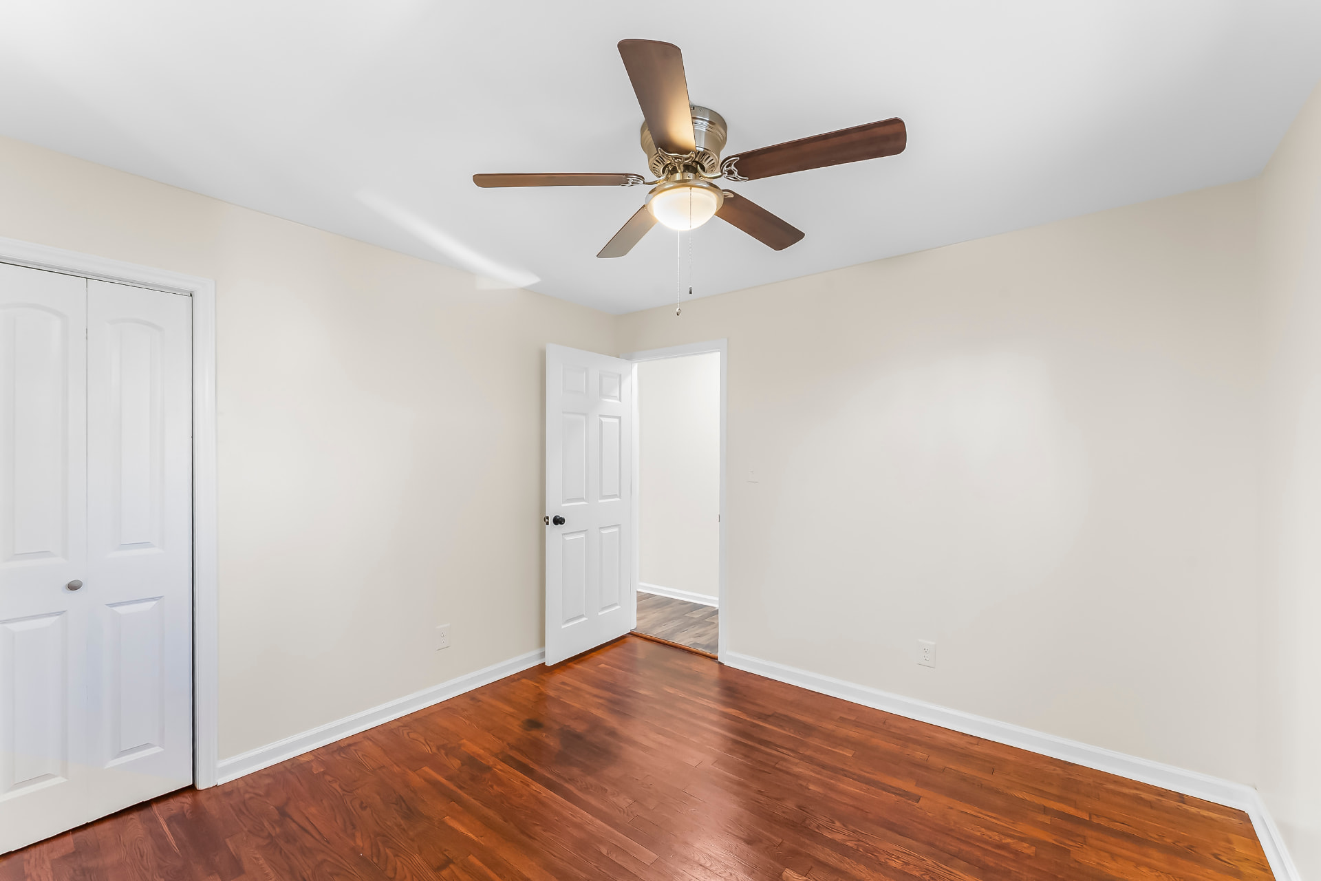 Bedroom with refinished hardwood floors, closet doors, and ceiling fan