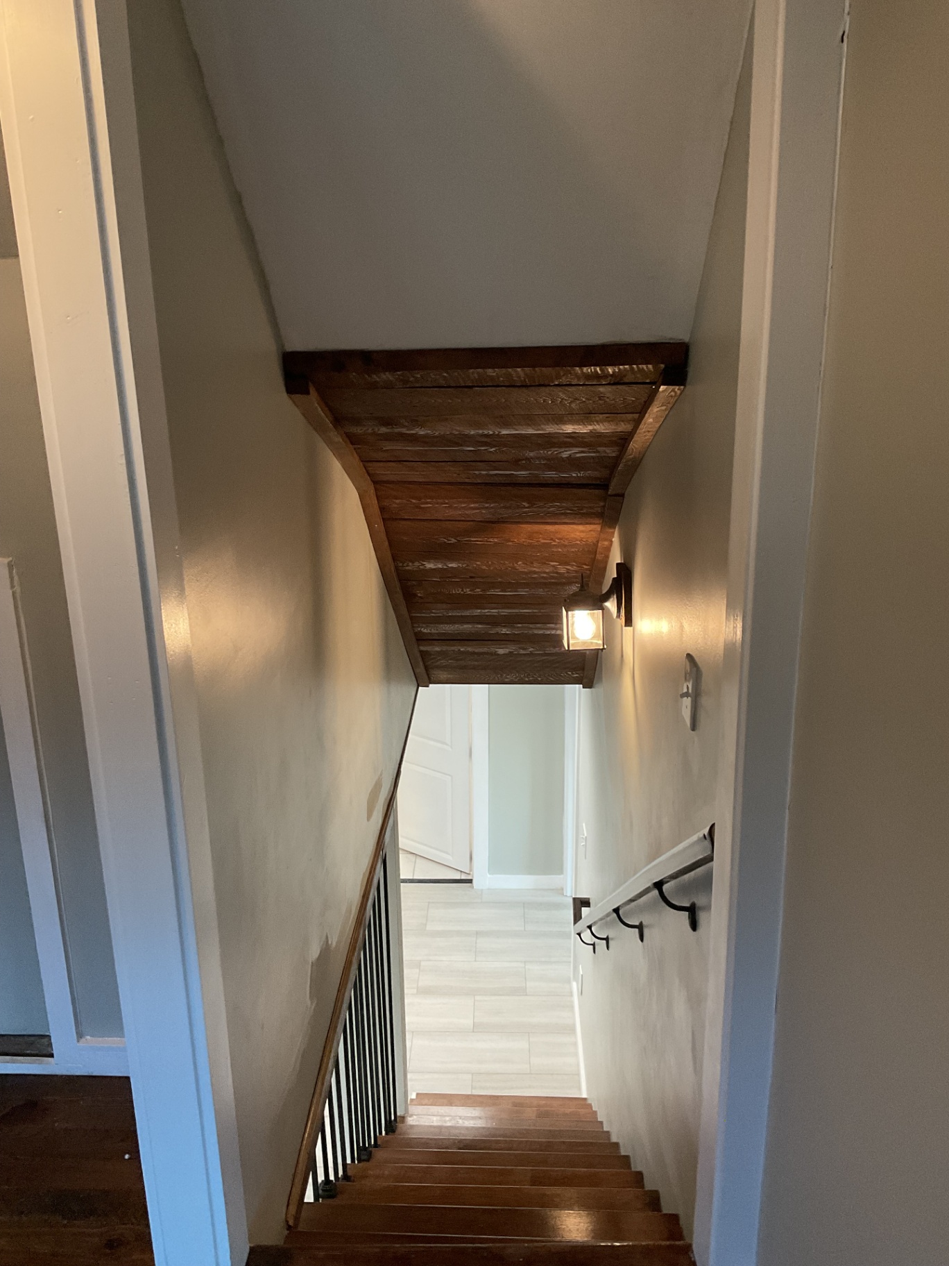 Stairwell with stained wood treads, iron balusters, wood plank ceiling detail, and sconce lighting