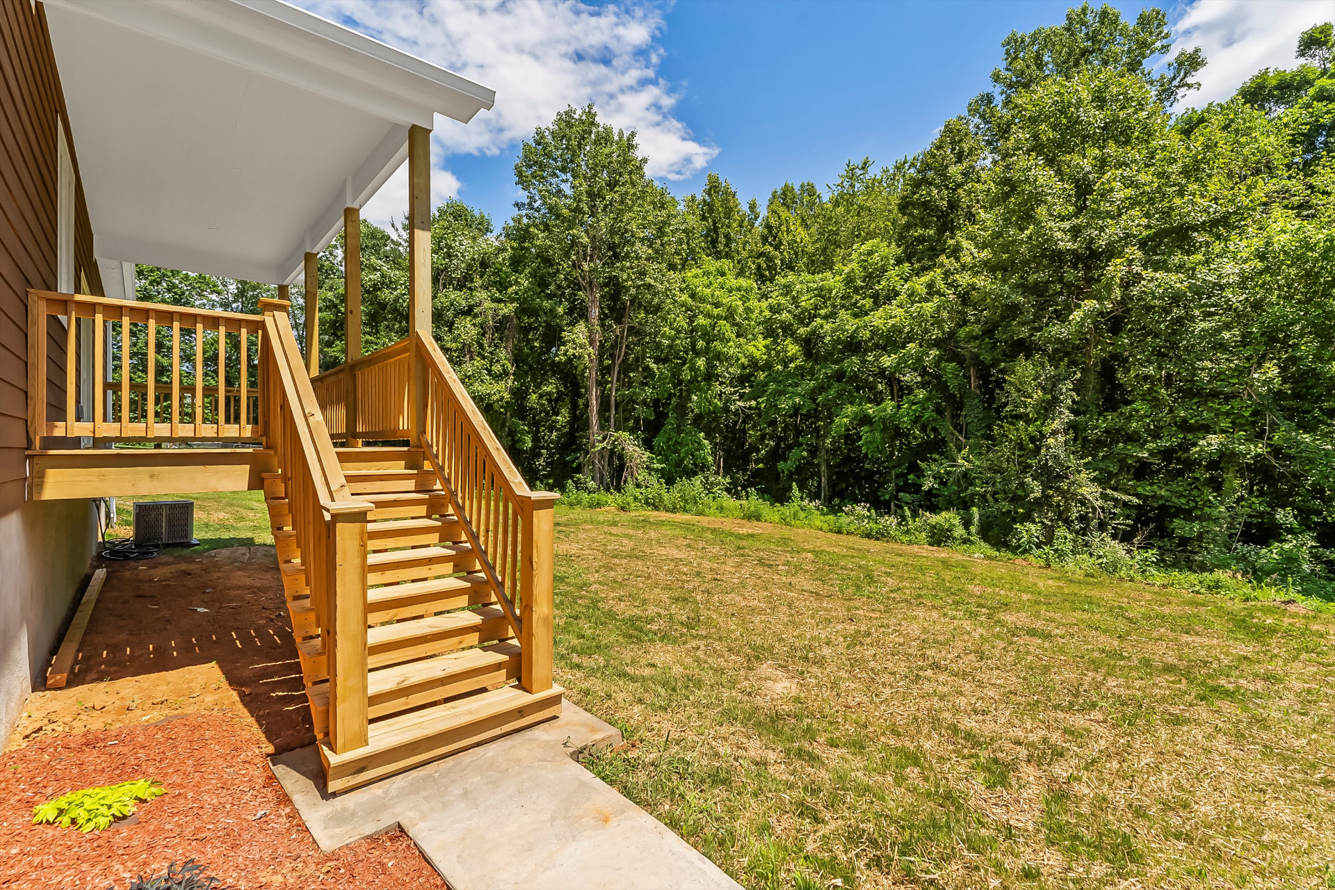 New pressure-treated deck stairs leading down to a concrete pad and mulched bed