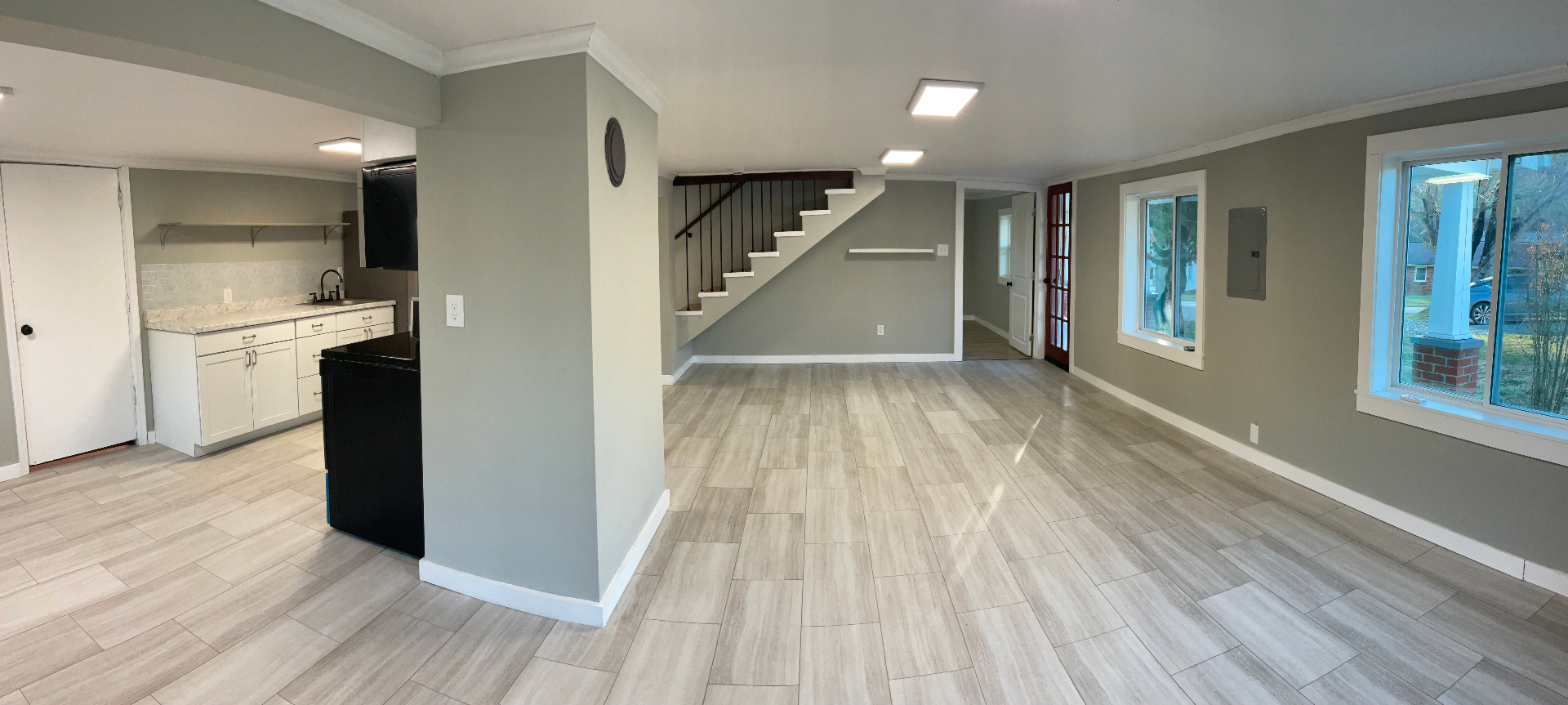 Wide view of the remodeled open floor plan with kitchenette, staircase, and French door entry