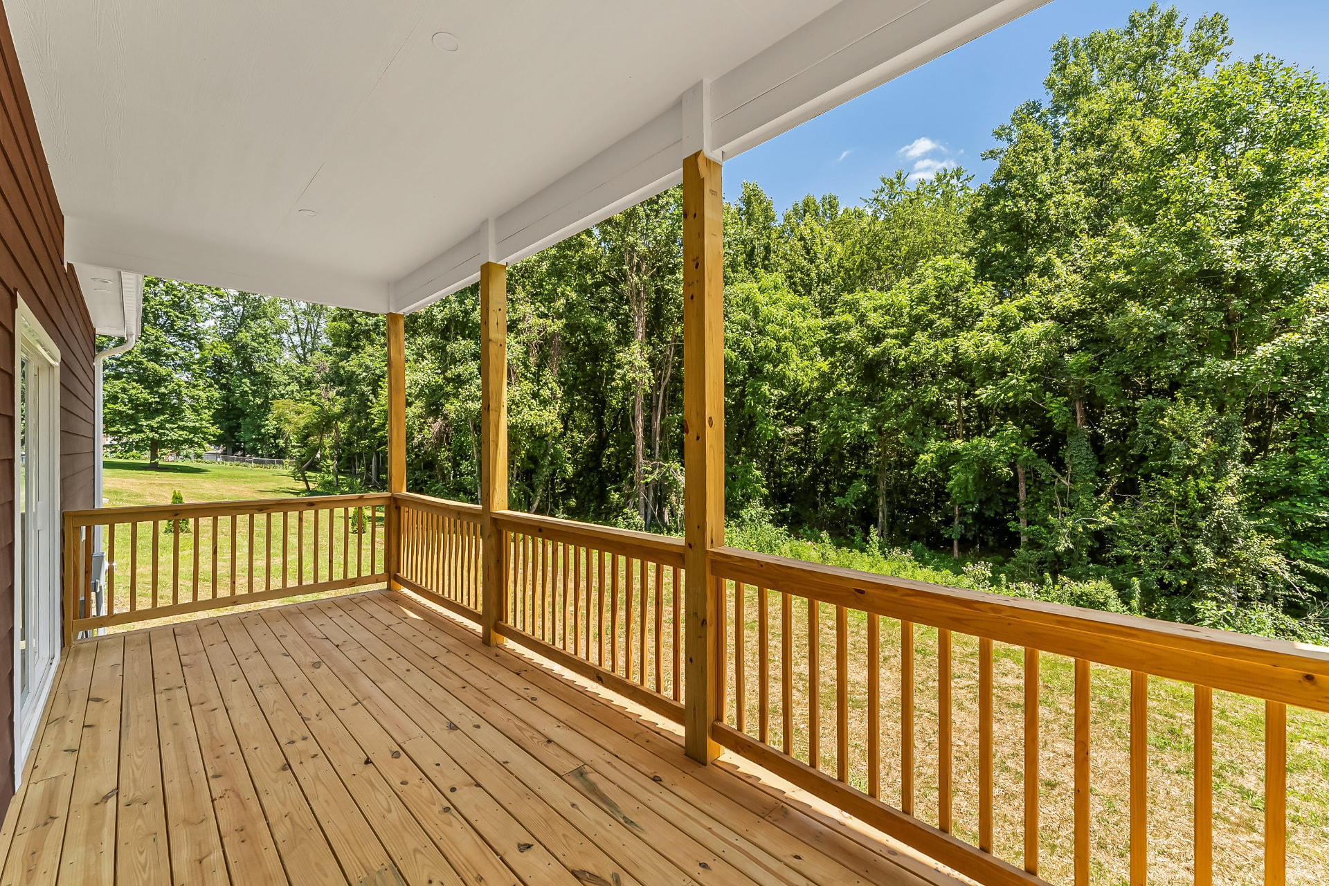 Covered rear deck with wood railing overlooking the wooded back yard