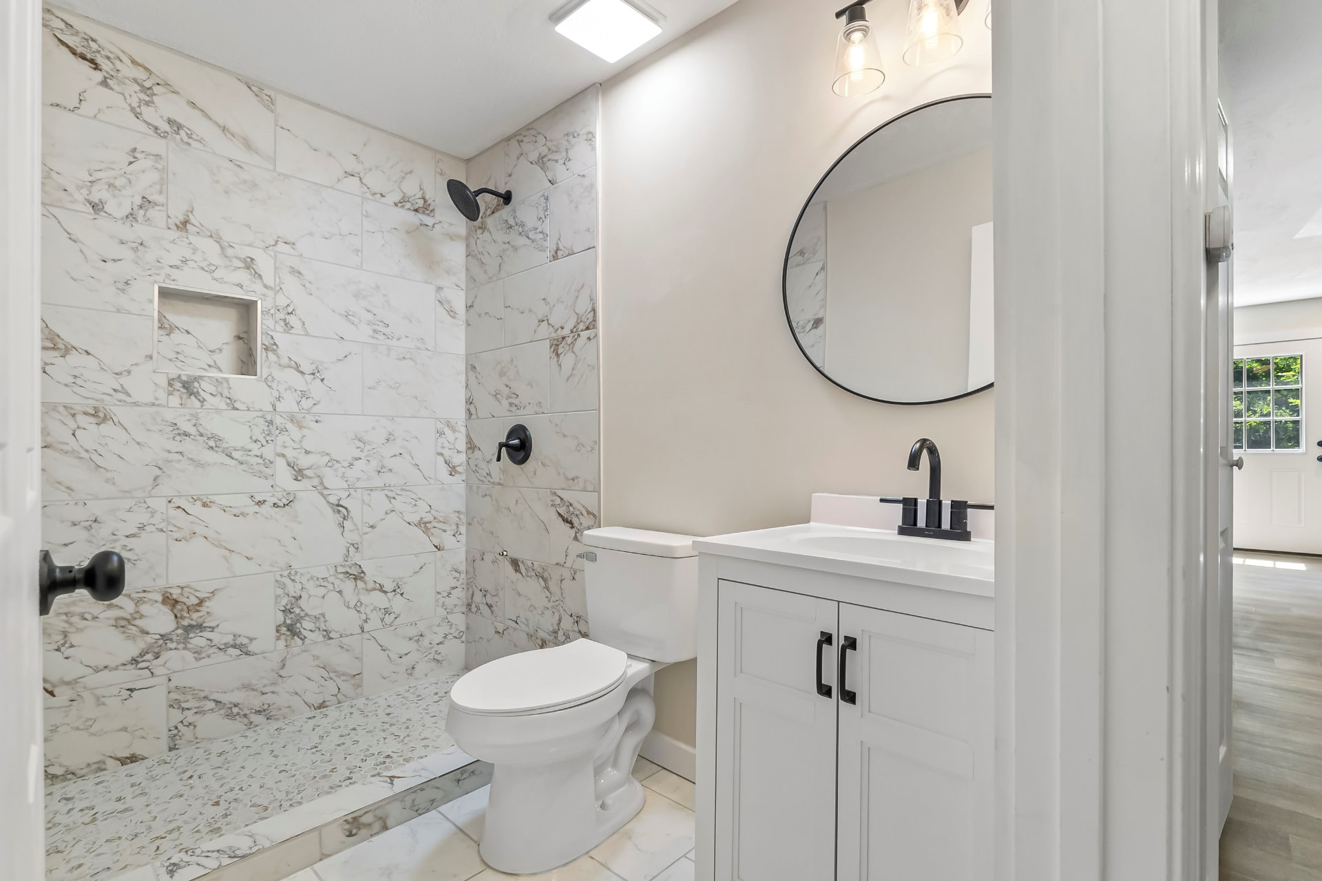 Renovated bathroom with marble-look tiled walk-in shower, round mirror, and matte black fixtures