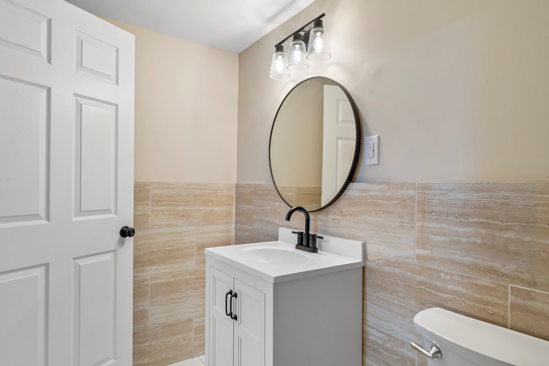 New basement bathroom with tiled walls, white vanity, round mirror, and black fixtures