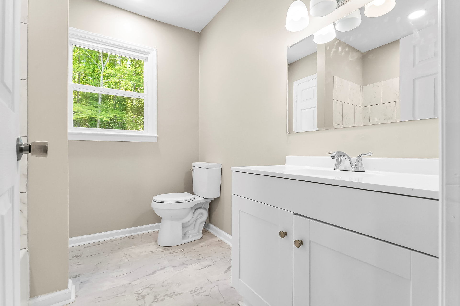 Full bathroom with new vanity, vanity lighting, tiled tub surround, and marble-look floor tile