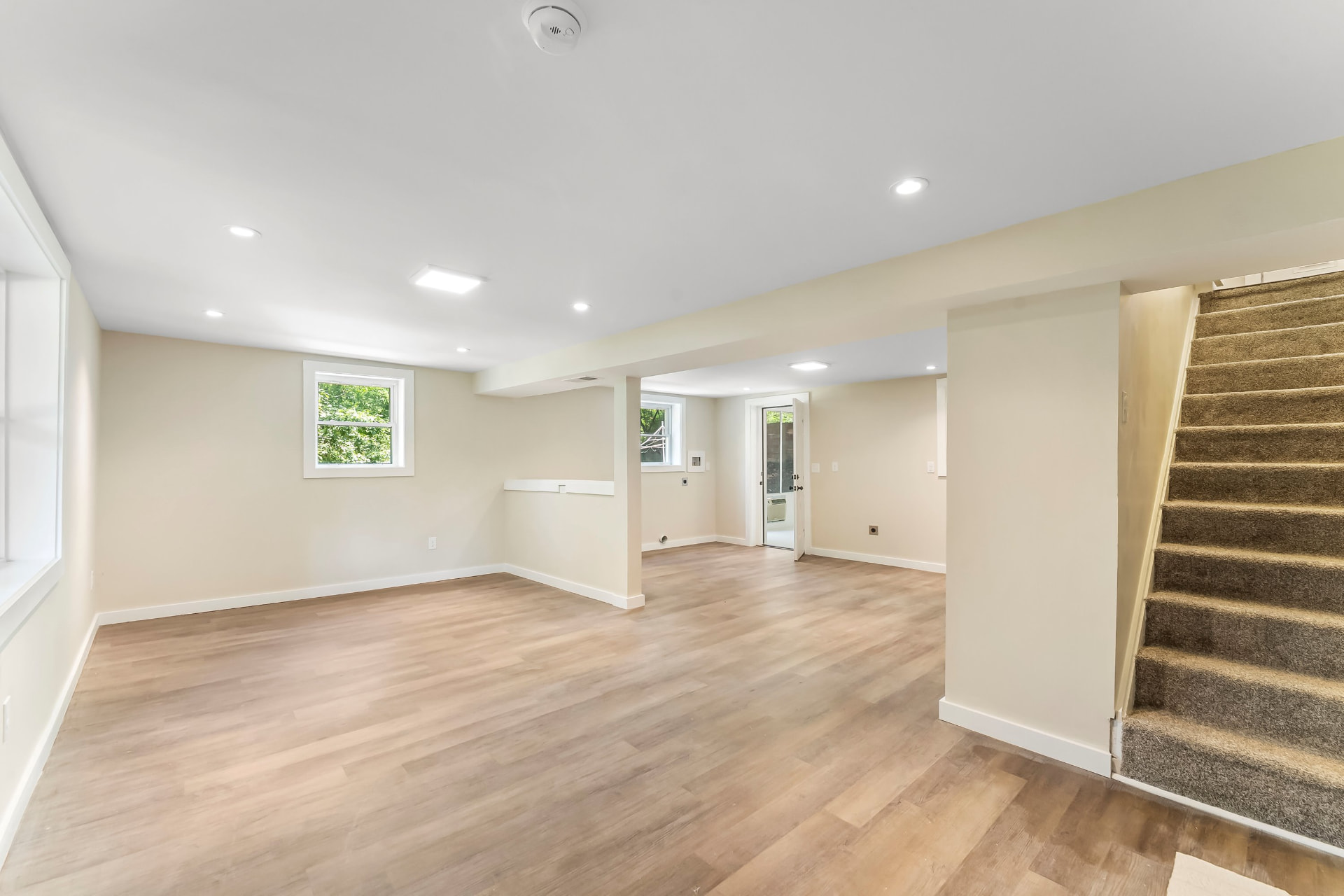 Finished basement living area with new flooring, recessed lighting, and stairs to the main level