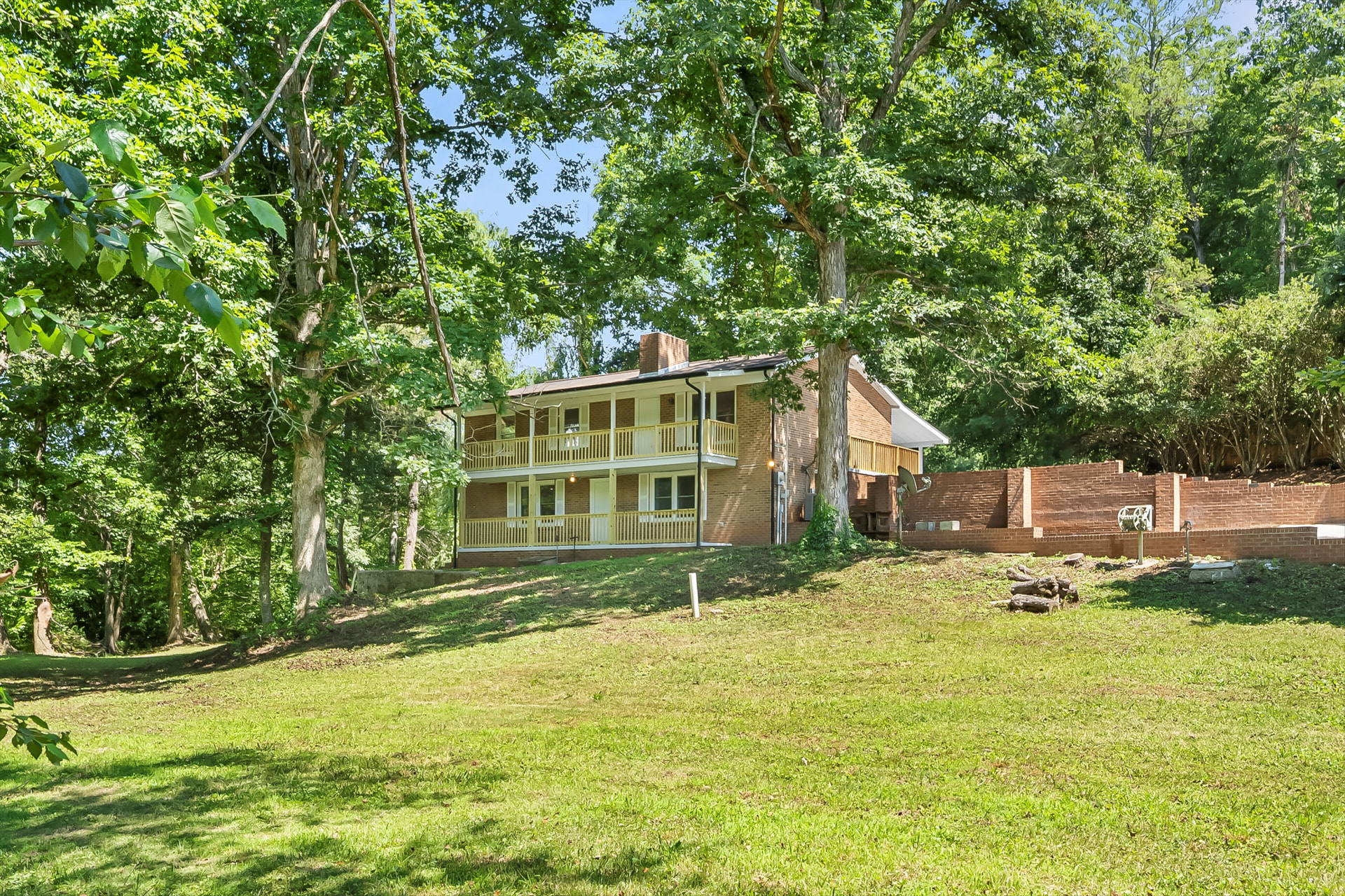 Rear view of the brick home showing stacked porches, new railings, and cleared, regraded yard