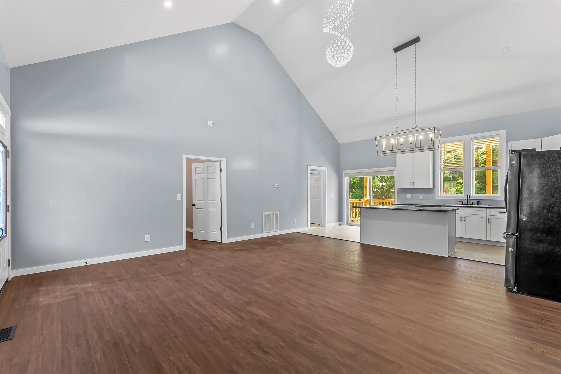 Open living area with vaulted ceiling, wood-look flooring, and view into the new kitchen