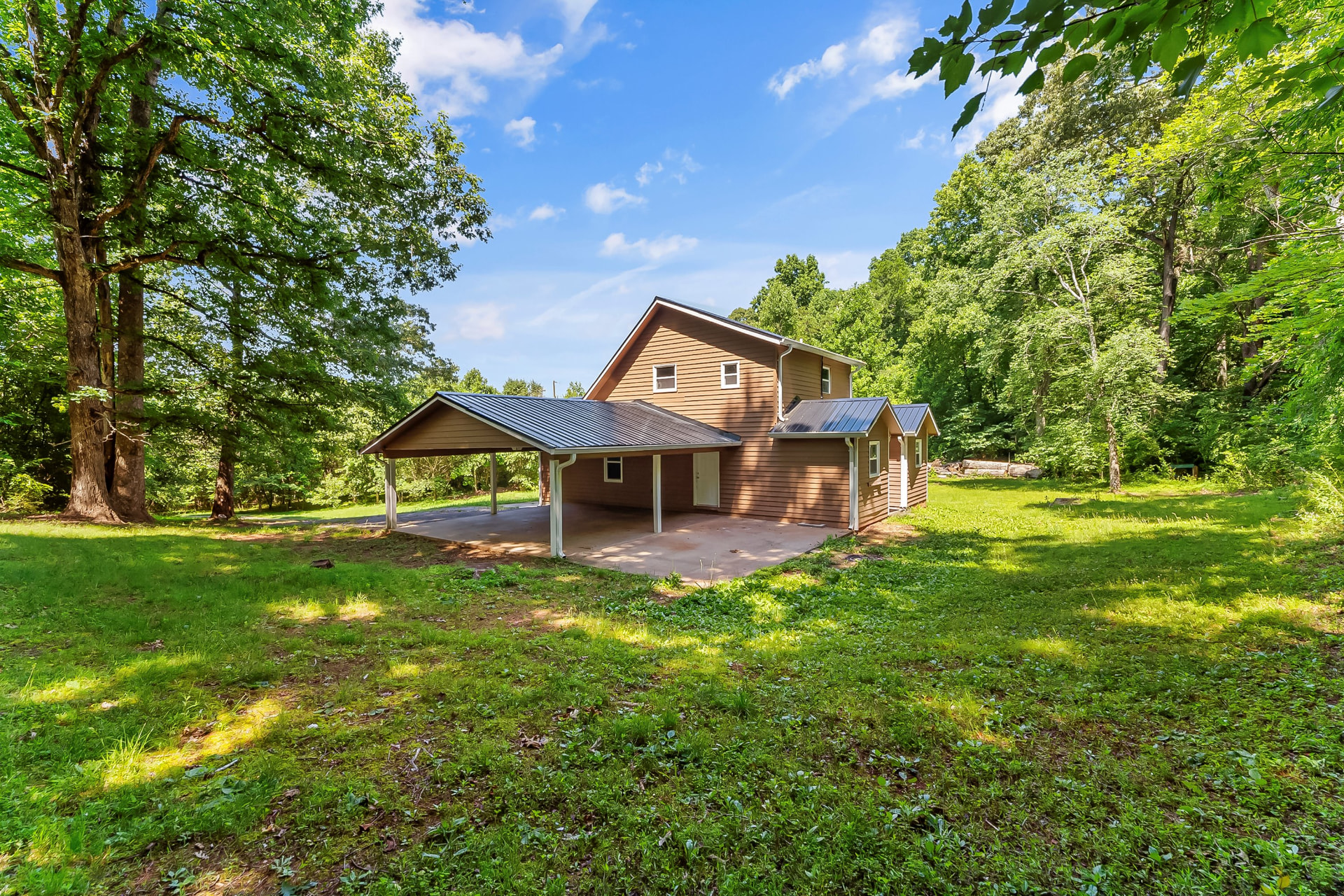 Rear exterior view of the remodeled home showing the carport, metal roofing, and open yard