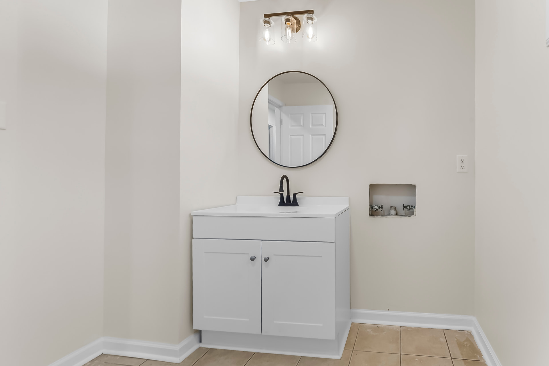 Bathroom vanity with round mirror, gold sconce light, and black faucet