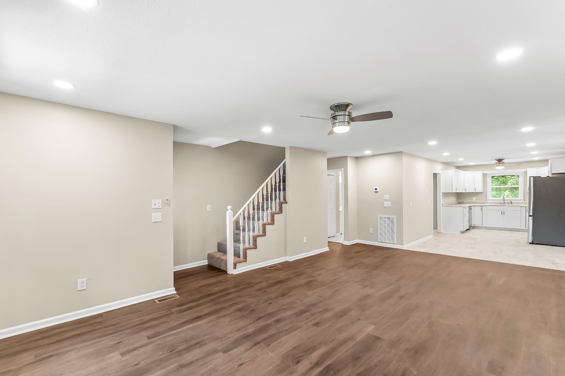 Open living room with new wood-look flooring, ceiling fan, and view into the remodeled white kitchen