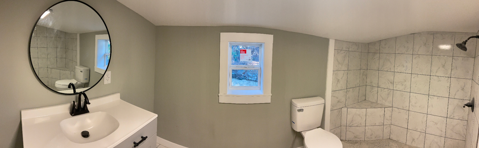 Remodeled bathroom with tiled walk-in shower, round mirror, and matte black fixtures