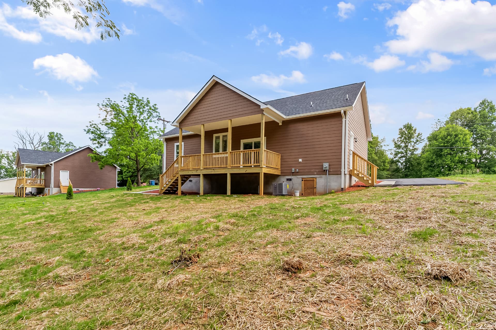 Rear view of the finished home with covered deck, stairs, and freshly seeded yard