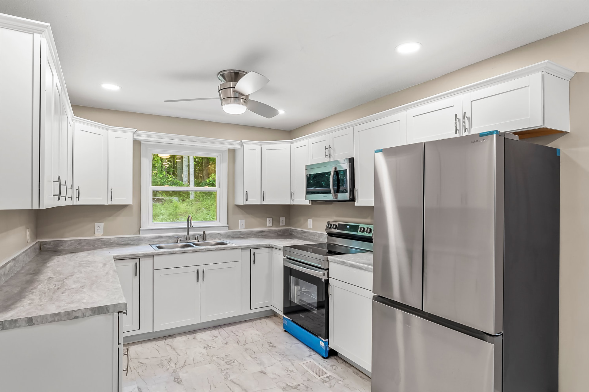 Remodeled kitchen with white shaker cabinets, marbled countertops, stainless appliances, and tile flooring