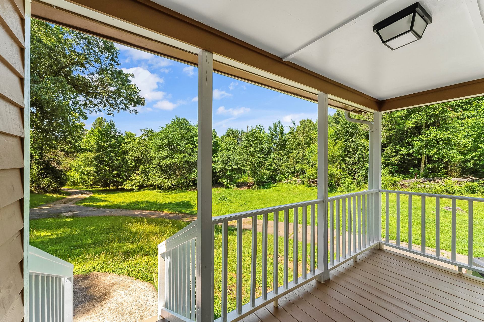 Covered front porch with new decking, white railings, and wooded views