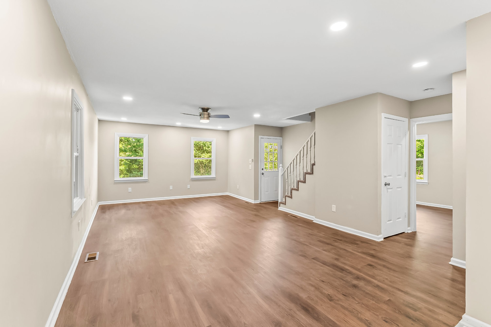 Bright open living area with fresh paint, recessed lighting, new windows, and staircase
